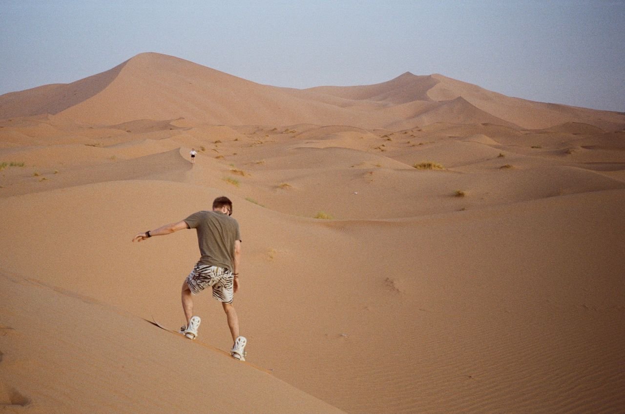 Turista haciendo sandboard bajando duna gigante en Merzouga