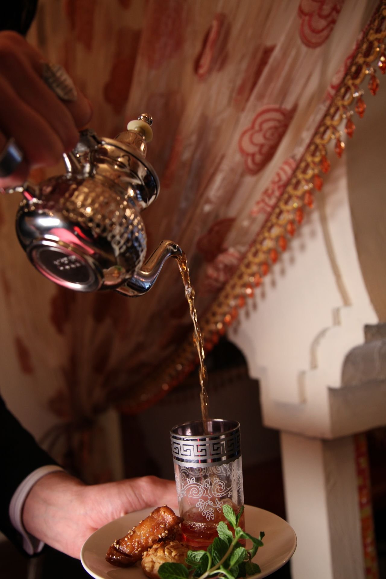 Tetera de metal tradicional sirviendo té con menta sobre un vaso decorado